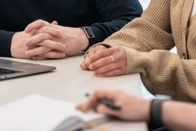 Close-up of three people sitting at a table in a meeting, with hands visible